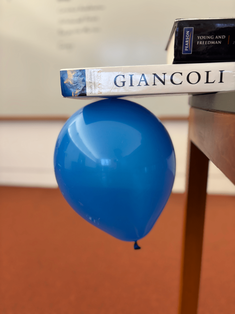 a blue balloon is hanging beneath a physics textbook